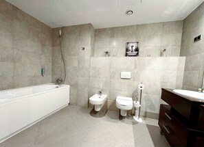 Een moderne badkamer met een bad, twee toiletten, een bidet en een wastafel met spiegel.