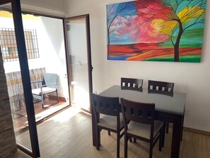Un coin repas avec une table et des chaises, un tableau accroché au mur et une vue sur le balcon extérieur.