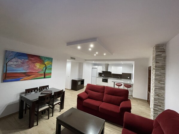 Un salon moderne avec un canapé rouge, une table à manger avec des chaises, et une cuisine en arrière-plan.