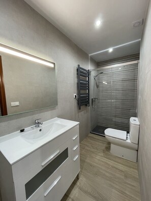 Une salle de bain moderne avec un meuble-lavabo blanc, un grand miroir, une cabine de douche et des toilettes.