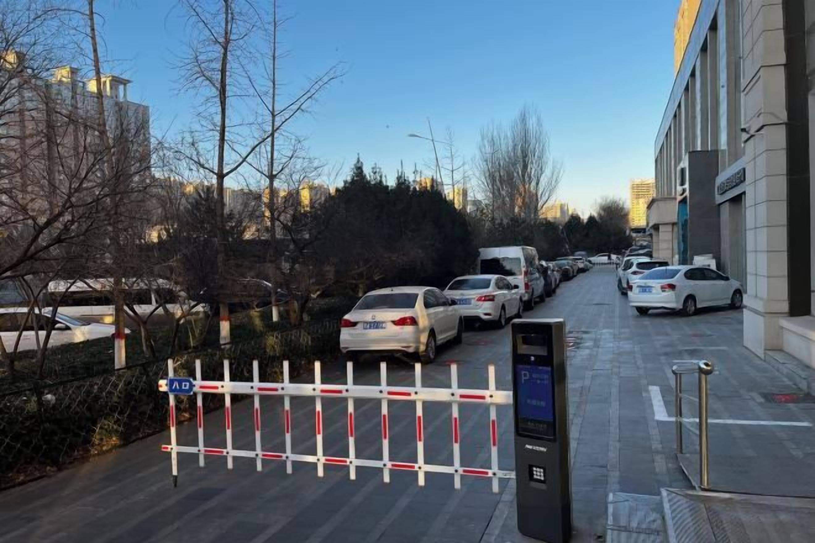 Un área de estacionamiento con autos, una entrada con portón y un edificio al fondo.