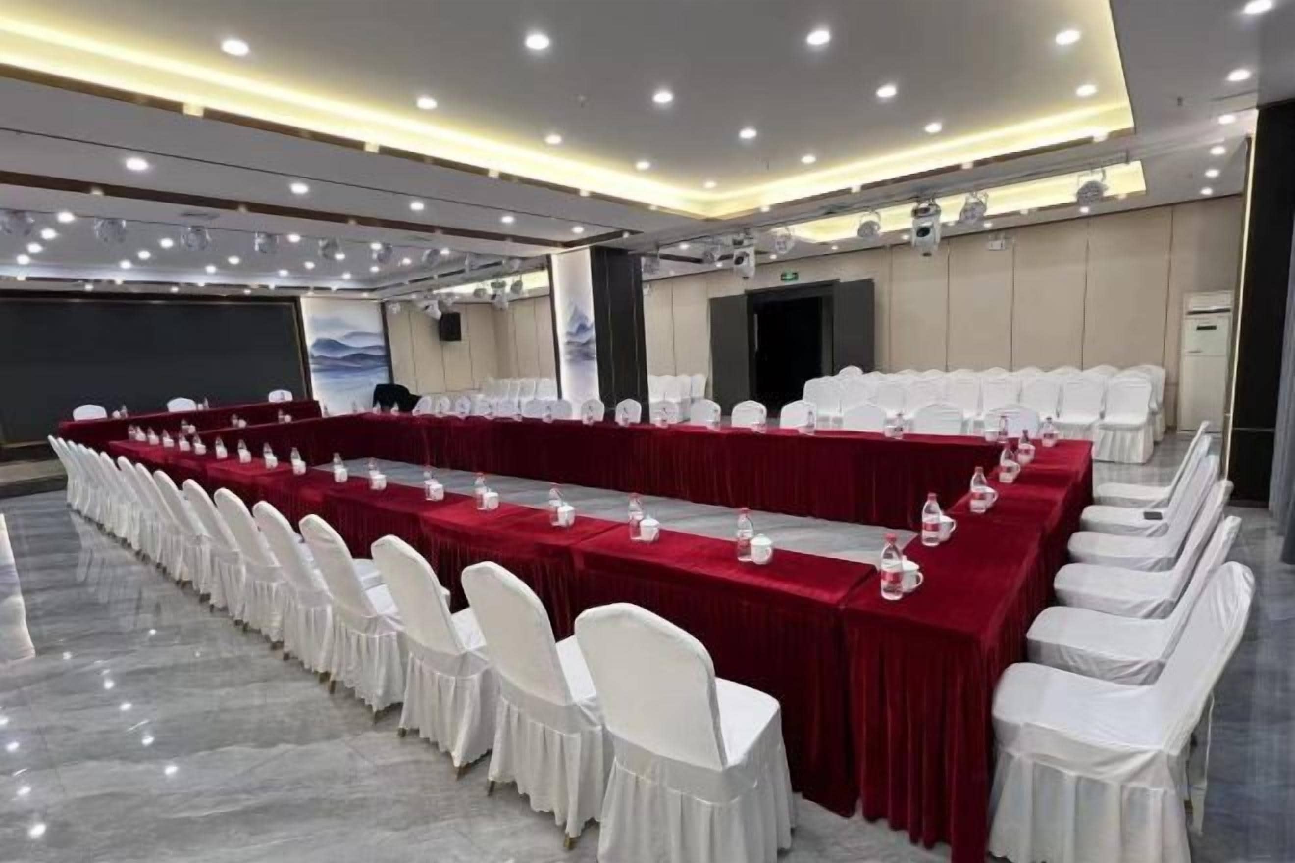 Une salle de conférence avec une longue table, des chaises blanches et une nappe rouge.
