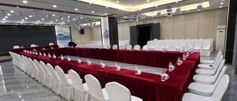 A conference room with a long table, white chairs, and a red tablecloth.
