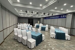 Un salón de conferencias con varias mesas y sillas, suelo de mármol e iluminación empotrada en el techo.