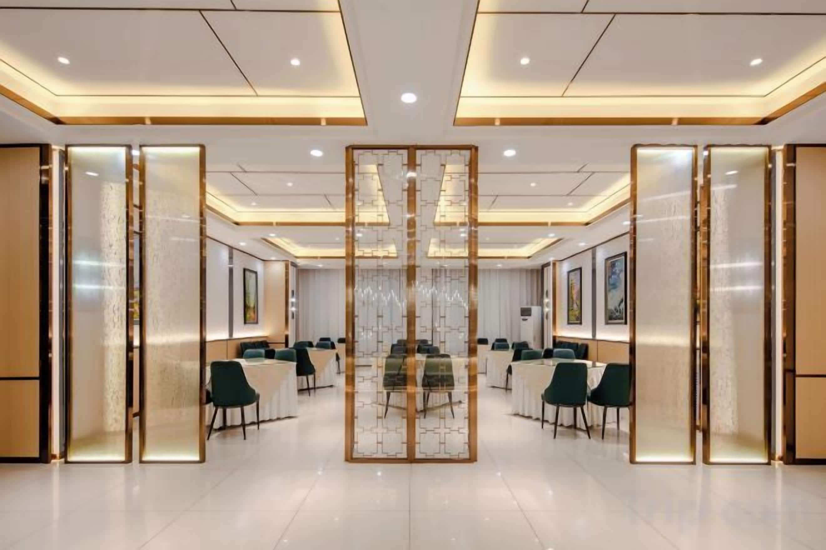 Une salle de conférence d’hôtel avec une table centrale entourée de chaises, séparée par des panneaux de verre et équipée de luminaires au plafond.