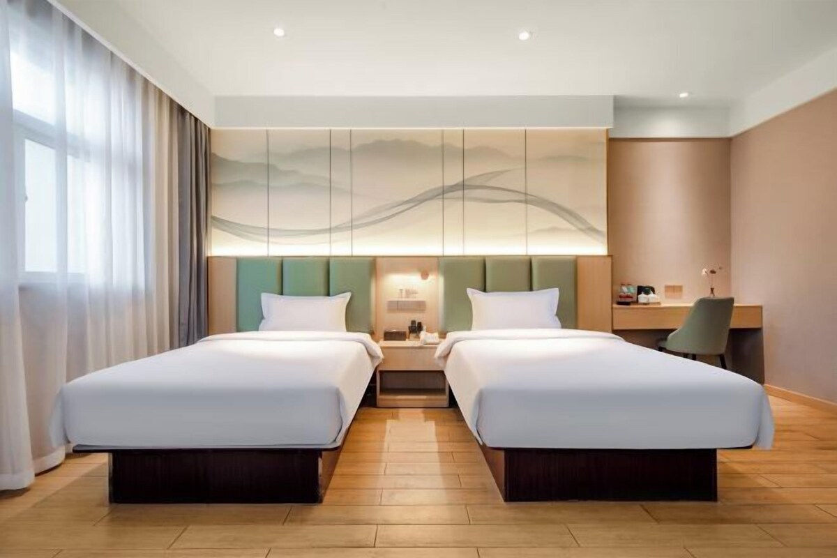 Habitación de hotel con dos camas, un escritorio, una silla y un ventanal con cortinas.