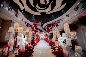 A corridor with a central pathway flanked by red floral arrangements and illuminated structures.