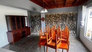 A dining area with a stone wall, wooden chairs, a wooden cabinet, and a ceiling fan. - Casa Mangostan (Savegre)