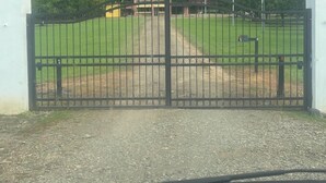 A gated area with a gravel path leading to a building with a yellow facade, surrounded by lush greenery and hills. - Casa Mangostan (Savegre)