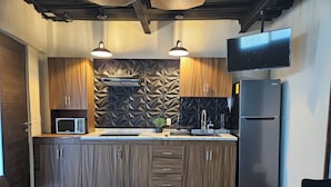 Una cocina moderna con armarios de madera, microondas integrado, refrigerador negro y televisor de pantalla plana en la pared.