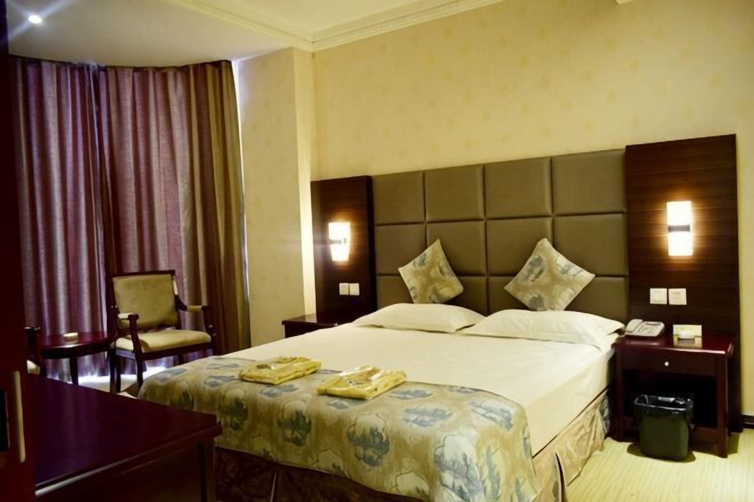 A hotel room with a large bed, two bedside tables, a chair, a desk, and a curtain.