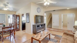 A spacious living room with a television, a dining area with a wooden table and chairs, a staircase, and a hallway leading to a door. - Best Pet Friendly Home In Bullhead City (Bullhead City)