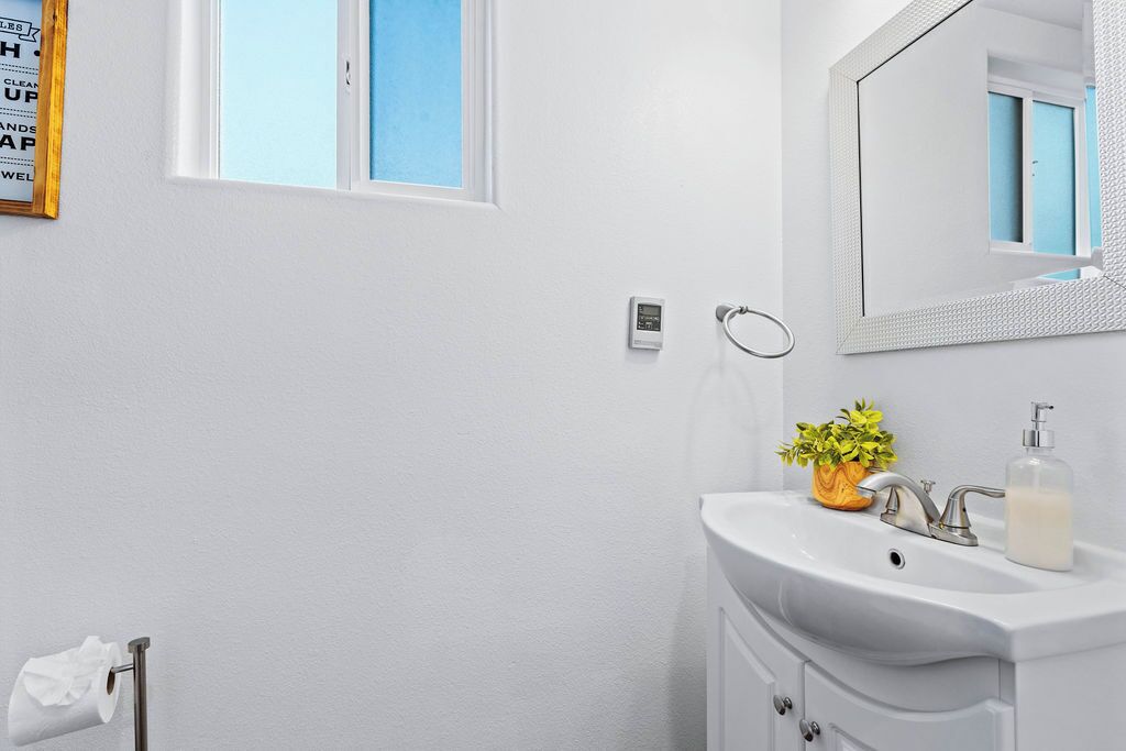 A bathroom with a white sink, a mirror, a window, and a towel rack.