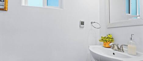 A bathroom with a white sink, a mirror, a window, and a towel rack.