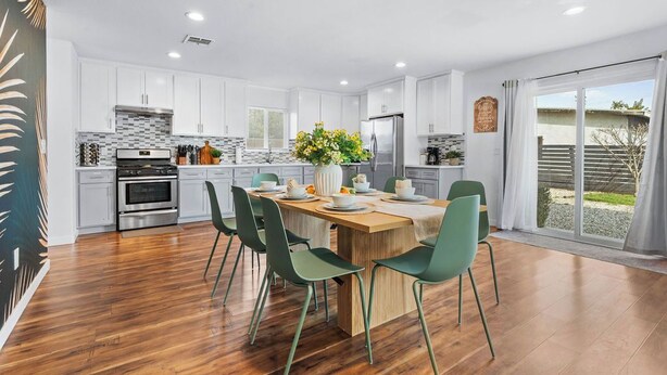 A modern kitchen with white cabinets, a wooden island, and a dining area with green chairs. - Wonderful Home near DTLA/Crypto Arena/Universal Studio (Los Angeles)