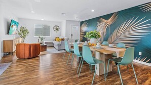 A modern dining area with a wooden table, teal chairs, and a large wall mural. - Wonderful Home near DTLA/Crypto Arena/Universal Studio (Los Angeles)