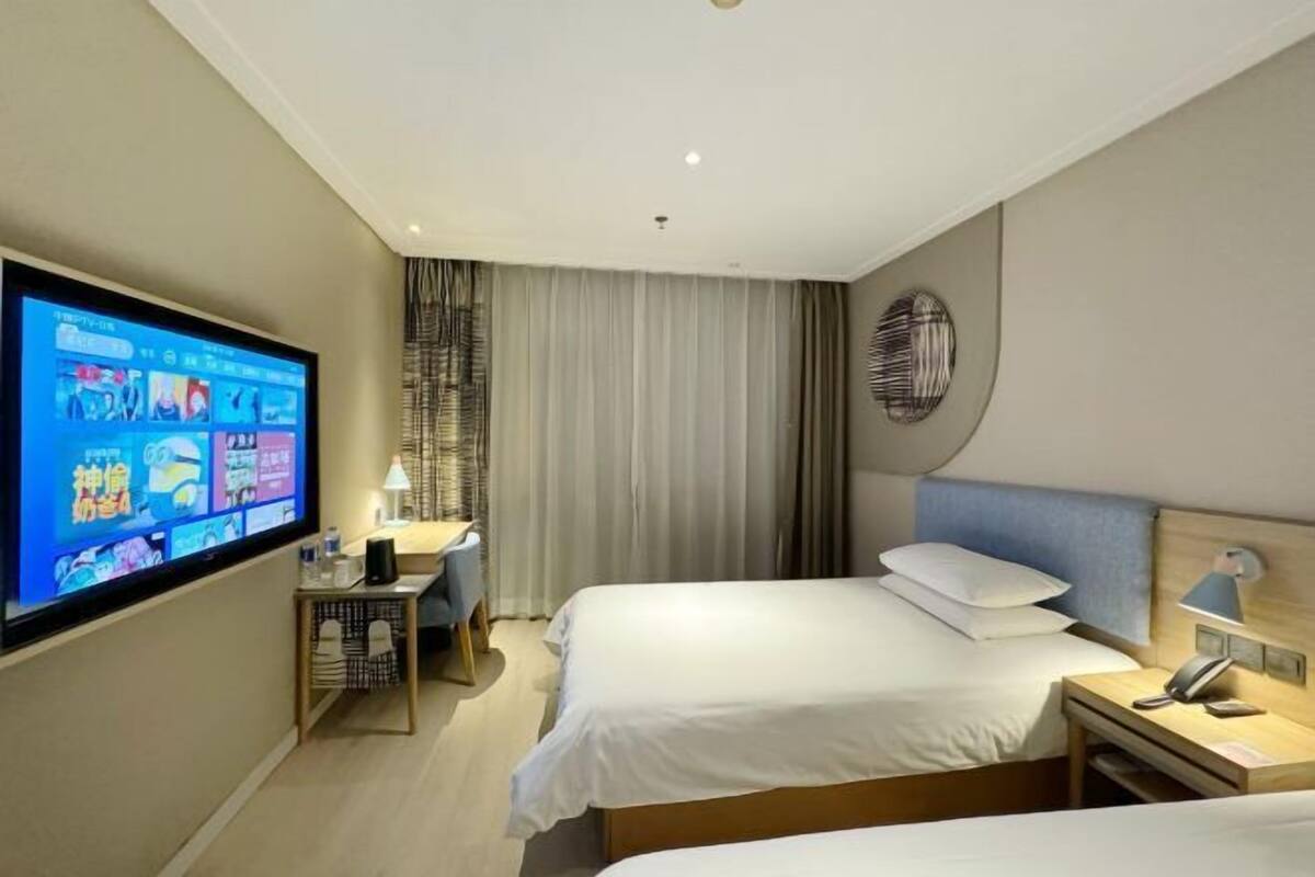 A hotel room with two beds, a desk, a television, and a wall-mounted light fixture.