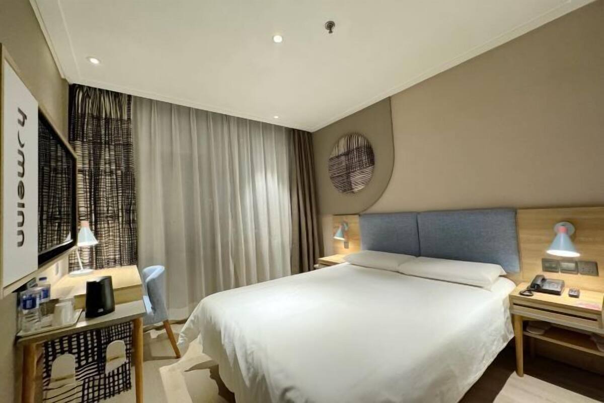A hotel room with a bed, bedside tables, a desk, a chair, a TV, and curtains.