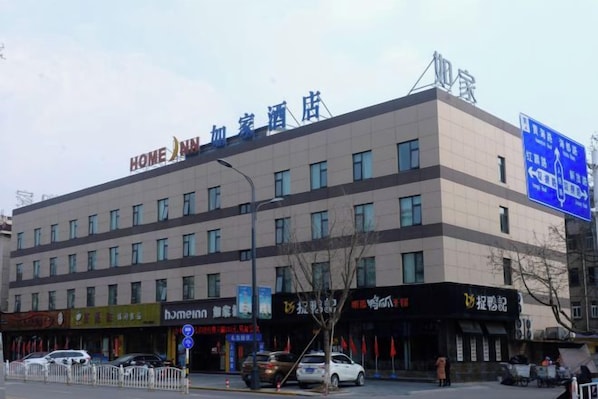 Un hotel de varios pisos con un letrero que dice 'HOME INN' y varios comercios en la planta baja.