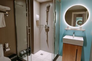 Un baño moderno con ducha de mampara de vidrio, un lavabo con espejo y un perchero para toallas.