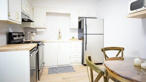 A modern kitchen with white cabinets, a stainless steel refrigerator, a microwave, and a wooden dining table with chairs. - Somerset- Luxury Condominium in Birmingham (Birmingham)