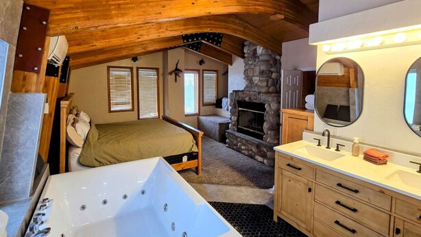 Un dormitorio acogedor con una cama grande, una chimenea de piedra y un baño con bañera y tocador.