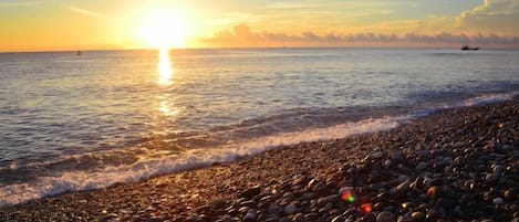 A beach with pebbles and a sunset over the water.