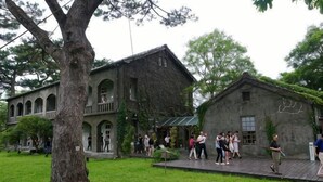 A building with a large tree in front, a grassy area, and a group of people. - Ocean Hotel (Hualien)