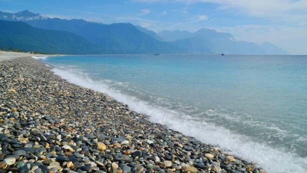 A pebbled beach with clear water and mountains in the background. - Ocean Hotel (Hualien)