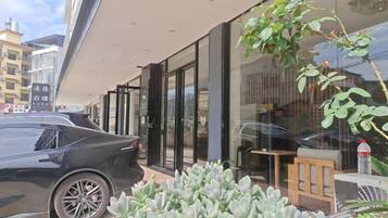 A modern building with a glass facade, a car parked outside, and a small outdoor seating area.