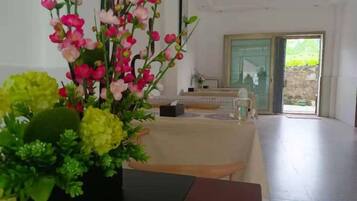 A room with a dining table, chairs, a vase of flowers, and a sliding glass door leading to an outdoor area.