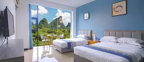 A hotel room with two beds, a desk, a TV, and a large window with a mountain view.