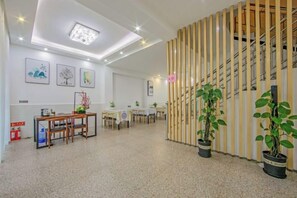 A hotel lobby with a reception desk, seating area, potted plants, and a staircase.