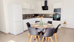A modern kitchen with white cabinets, a black range hood, and a dining area with a round table and black chairs. - Cosy, spacious house near Puy du Fou (La Boissière-de-Montaigu)