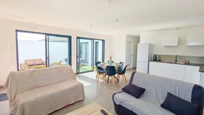 A modern living room with a sofa, a coffee table, and a dining area with chairs and a table. - Cosy, spacious house near Puy du Fou (La Boissière-de-Montaigu)