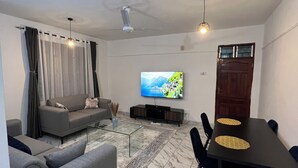 Una sala de estar con sofá, televisor, mesa de comedor y sillas.