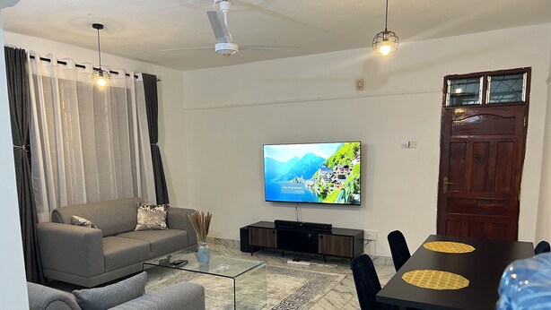 Una sala moderna con sofá, una mesa de centro, televisor y un comedor con sillas.