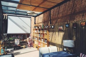 Een kamer met een grote boekenkast, een witte bank, een tafel met een lamp en een projectiescherm.