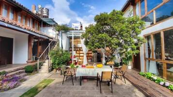 A patio with a table and chairs, surrounded by a garden and a building with large windows.