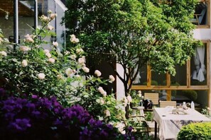 A garden with a table and chairs, a tree, and purple flowers.