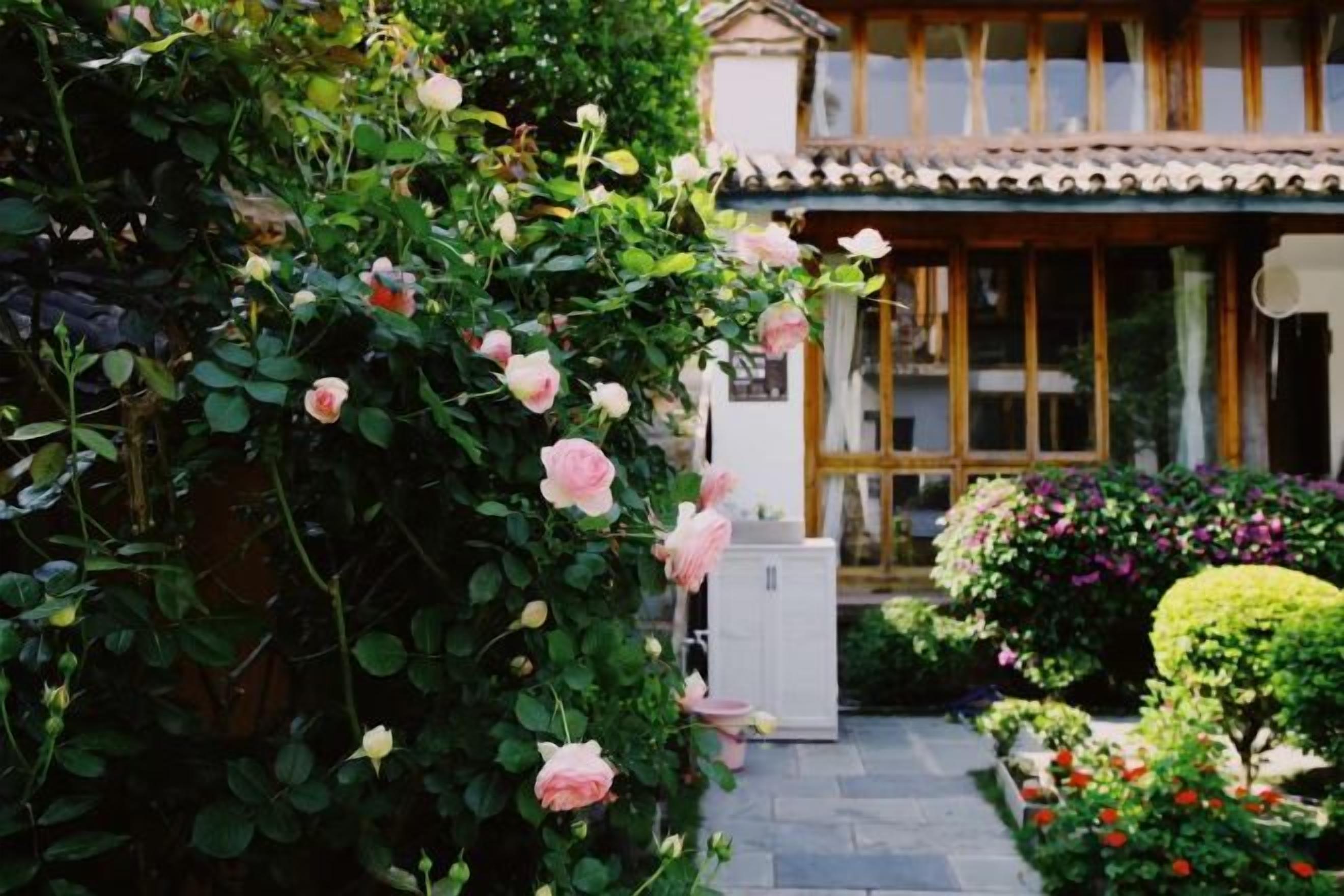 A traditional Japanese-style building with a covered entrance, a garden with various plants and flowers, and a pathway leading to the entrance.