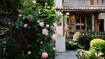 A traditional Japanese-style building with a covered entrance, a garden with various plants and flowers, and a pathway leading to the entrance.