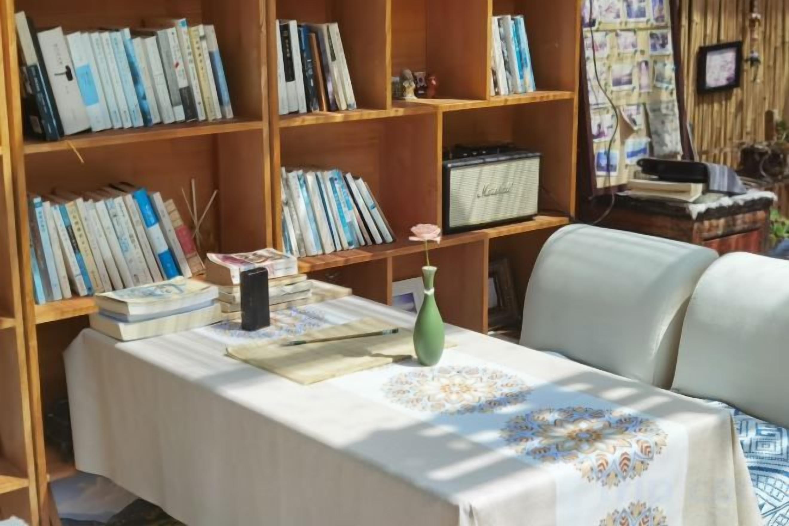 A room with a table covered by a tablecloth, a bookshelf filled with books, and a chair.