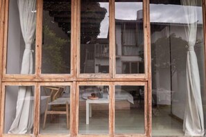 A room with a wooden-framed window, a small table with a chair, and a bed.