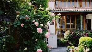 Uma casa japonesa tradicional com um jardim, apresentando um roseiral e diversas outras plantas.