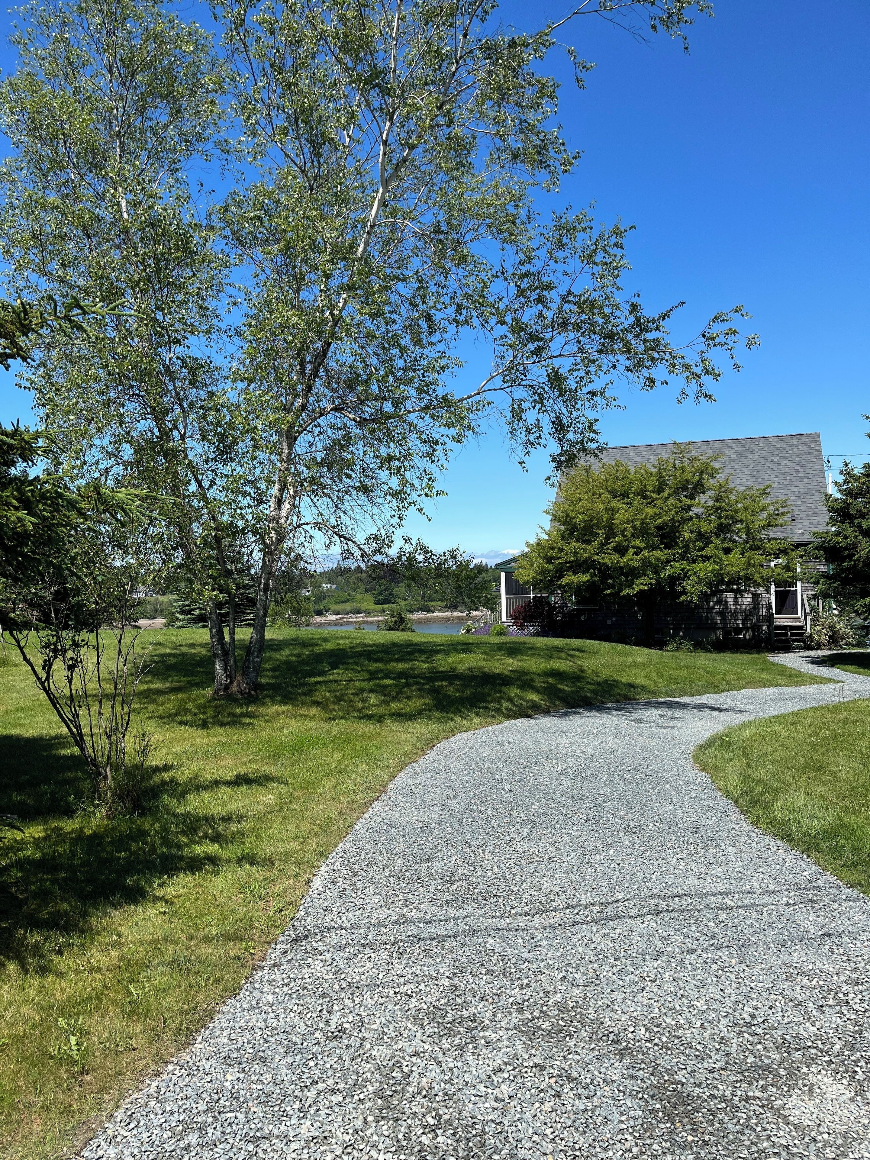 A gravel path leading through a grassy area with trees and a building in the background.