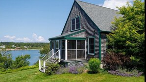 A house with a covered porch, a small window, and a view of a lake. - Charming 3-bedroom waterfront cottage in Tremont with spectacular sunsets. (Tremont)