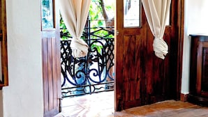 Un espacio interior con una puerta de madera, piso de baldosas y vista a zonas verdes.