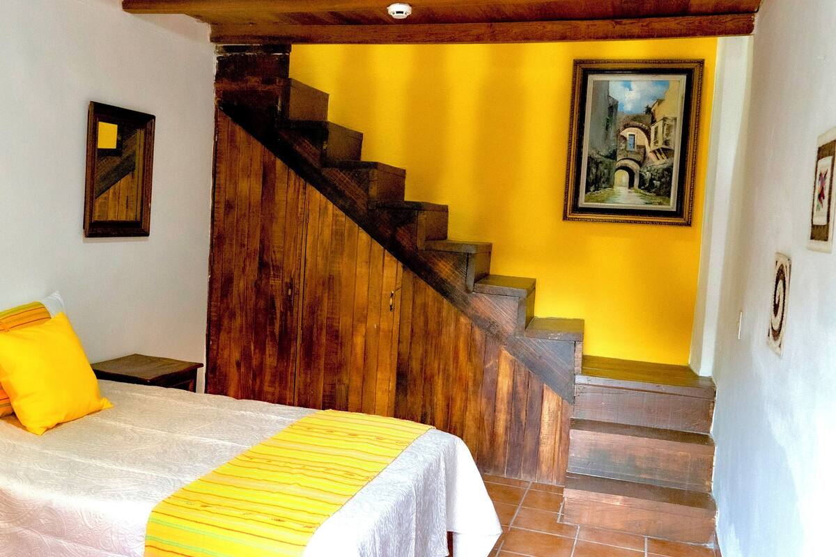 Une chambre avec un lit, un escalier en bois et un tableau accroché au mur.