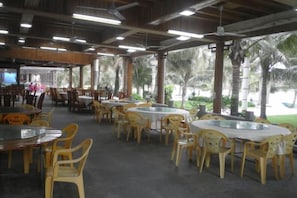 Un espace de restauration intérieur avec des tables et des chaises rondes, un toit abrité et une vue sur les palmiers.
